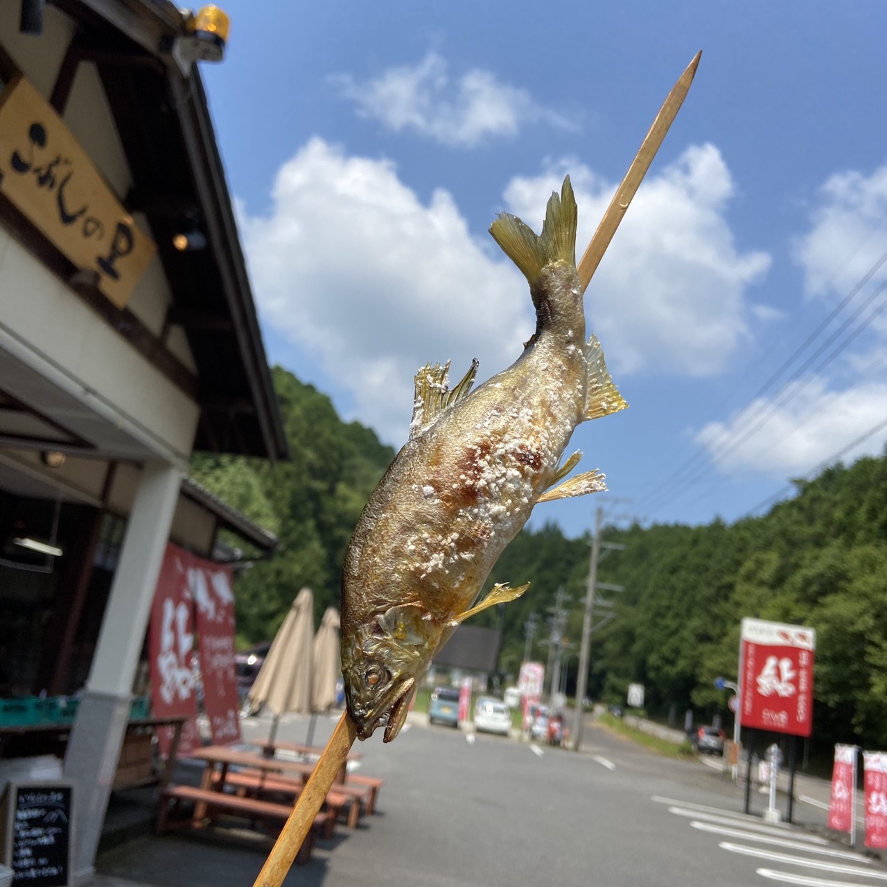 こぶしの里の店舗前で撮影した、夏空と焼きたての鮎塩焼き